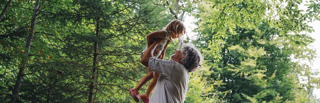 grandpa lifting grandchild high up in the air outside in green summer forest.